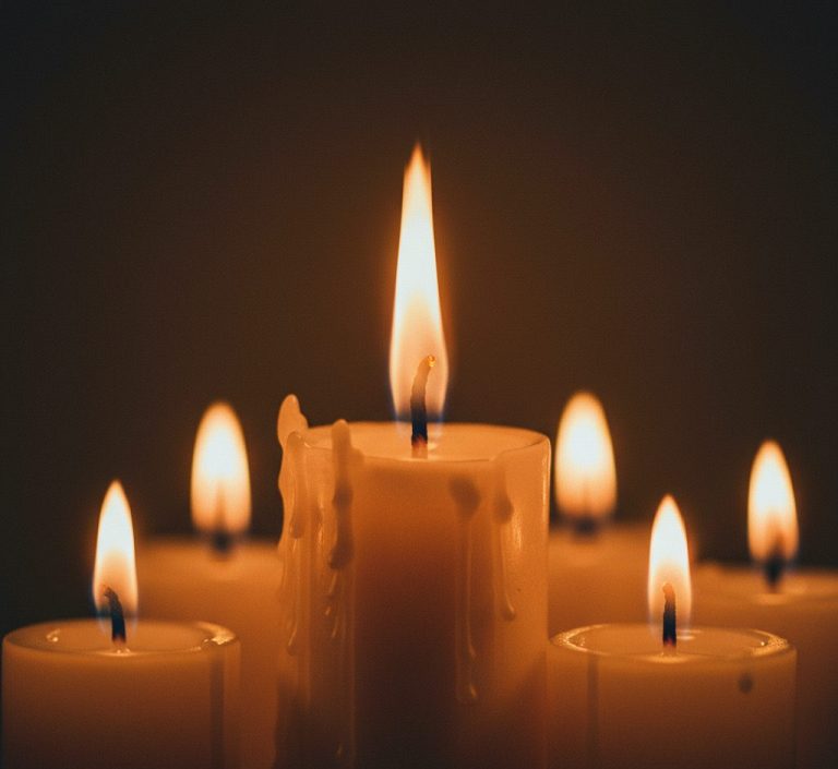 A candle burns with a steady flame, surrounded by the faint glow of other smaller candles suggesting the body’s intelligent energy conservation after weight loss.